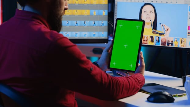 Photo editor learning from tutorial on green screen tablet while working in independent production company. Photographer watching online guide on mockup device about adjusting white balance