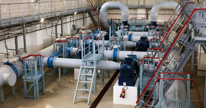 The industrial water pumping station features well-maintained pumps, pipes, and valves, brightly lit and showcasing precise engineering in efficient water management.