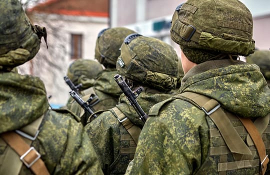 Several soldiers wearing camouflage uniforms stand in a row, holding guns and looking prepared for a mission. The background is blurred, highlighting their readiness and determination.