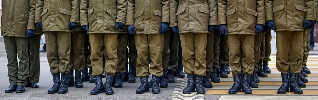 Army soldiers in uniform stand in formation on a concrete surface with yellow crosswalk lines. They wear combat fatigues and boots, showing discipline and readiness.