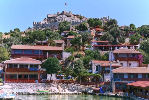 Charming Mediterranean village on Turkish coast with red-roofed houses, historic stone castle, and stunning sea views, perched on cliffs overlooking the azure waters of the Mediterranean Sea.