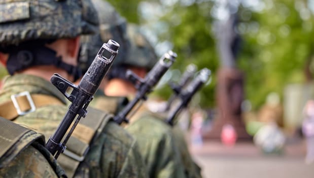 A soldier in full gear stands at attention with a rifle, wearing a helmet and camouflage uniform. Blurred background adds focus and determination to his readiness and vigilance.