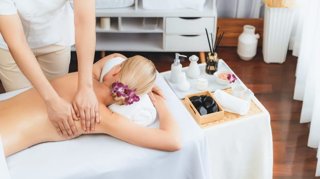 Caucasian woman customer enjoying relaxing anti-stress spa massage and pampering with beauty skin recreation leisure in day light ambient salon spa at luxury resort or hotel. Quiescent