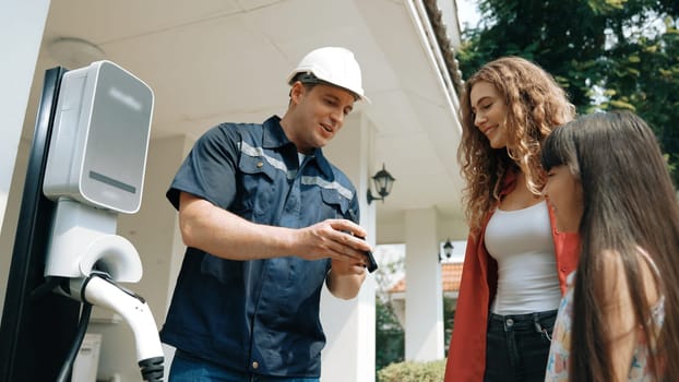 Technician install home EV charging station, providing service support for EV app on customer smartphone for monitoring charging status and set charging schedules at home. Synchronos