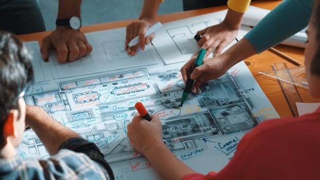 Top view of civil engineer team writing at blueprint at meeting table with color palettes. Group of smart diverse people planning and taking a note while manager looking at project plans. Symposium.