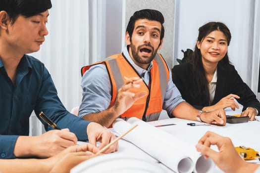 Diverse group of civil engineer and client working together on architectural project, reviewing construction plan and building blueprint at meeting table. Prudent