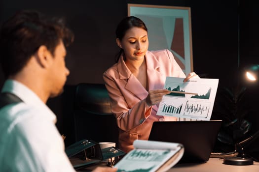 Focusing on sitting on pink suit woman presenting graph target on paperwork to explain customer market target graph report's business expansion to coworker while man holding paper to sign. Postulate.