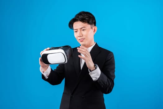 Smiling Asian businessman looking through VR connecting financial business report futuristic metaverse data analytics power bi technology virtual reality meta isolated blue copyspace. Contrivance.