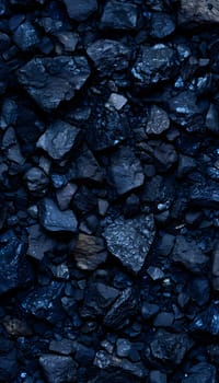A closeup of a pile of black rocks with electric blue patterns, sitting on dark soil near a liquid water source. The rocks contrast with the surrounding metal road surface