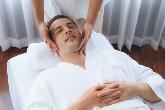 Caucasian man enjoying relaxing anti-stress head massage and pampering facial beauty skin recreation leisure in dayspa modern light ambient at luxury resort or hotel spa salon. Quiescent