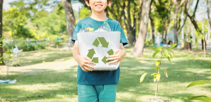 Cheerful young asian boy holding recycle symbol bin on daylight natural green park promoting waste recycle, reduce, and reuse encouragement for eco sustainable awareness for future generation. Gyre