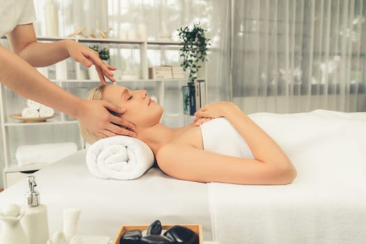 Caucasian woman enjoying relaxing anti-stress head massage and pampering facial beauty skin recreation leisure in dayspa modern light ambient at luxury resort or hotel spa salon. Quiescent