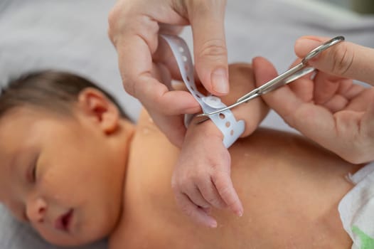 A woman cuts a tag from a newborn boy's hand with nail scissors. Close-up of hands