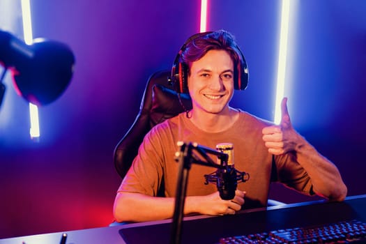 Host channel of gaming smart smiling streamer looking at camera pose gesture, live steaming on social media online in cyber gamer team skill players group at neon blue and pink light room. Pecuniary.