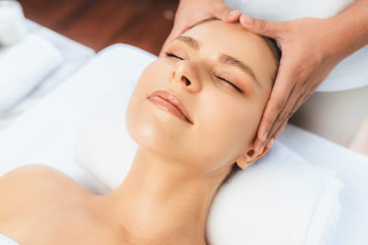 Caucasian woman enjoying relaxing anti-stress head massage and pampering facial beauty skin recreation leisure in dayspa modern light ambient at luxury resort or hotel spa salon. Quiescent