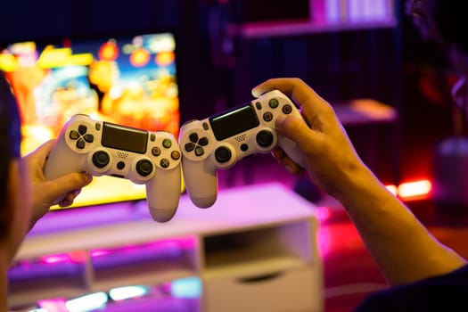 Close up of hands couple or friends joyful player video game on TV using to bring joysticks together for winner with blurry screen in studio room in neon cyber light at comfy living home. Postulate.