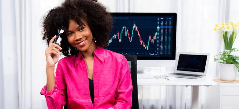 Analytical young African American businesswoman, a specialist in successful stock exchange trading, against dynamic data graph displaying marketing trend analysis on screen. Tastemaker.