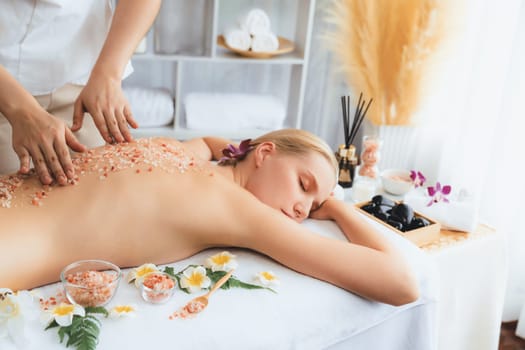 Woman customer having exfoliation treatment in luxury spa salon with warmth candle light ambient. Salt scrub beauty treatment in health spa body scrub. Quiescent