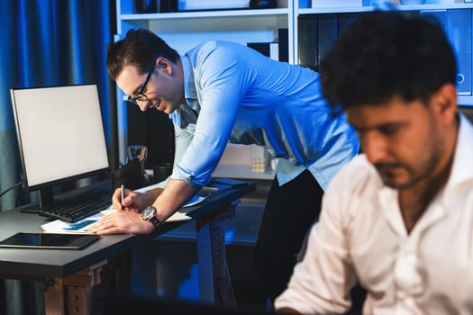 Colleagues concentrating on their job task at night home office behind desk while another man with thoughtful face solving to postpone the deadline of project at the blurred front side. Sellable.