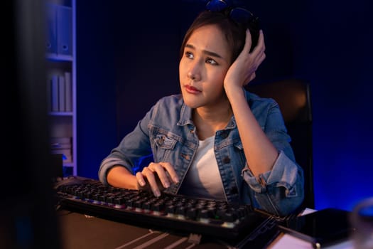 Stressful young beautiful asian creative looking on pc to search project creator social media online with planning channel strategy reach of more viewer home at neon modern office at night. Stratagem.