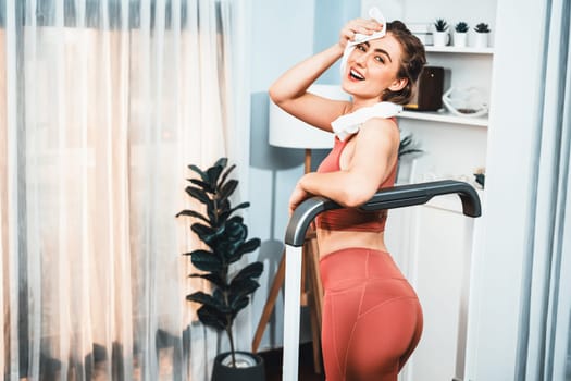 Athletic and sporty woman running on treadmill running machine during home body workout exercise session for fit physique and healthy sport lifestyle at home. Gaiety home exercise workout training.