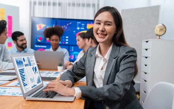 Portrait of happy young asian businesswoman with group of office worker on meeting with screen display business dashboard in background. Confident office lady at team meeting. Concord