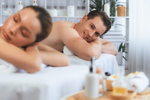 Blissful couple customer having exfoliation treatment in luxury spa salon with warmth candle light ambient. Salt scrub beauty treatment in health spa body scrub. Quiescent