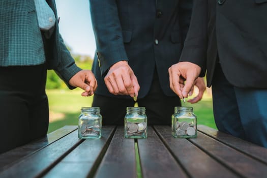 Business people put coin to money saving glass jar on outdoor table as sustainable money growth investment or eco-subsidize. Green corporate promot and invest in environmental awareness. Gyre