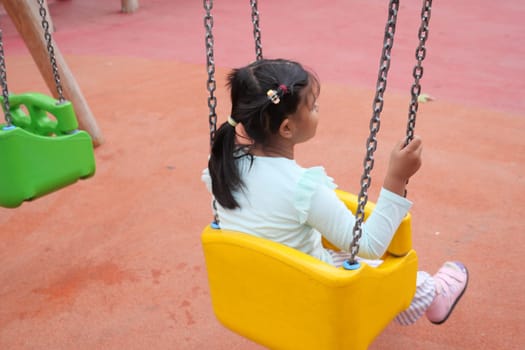 child having fun on a swing on the playground in public park