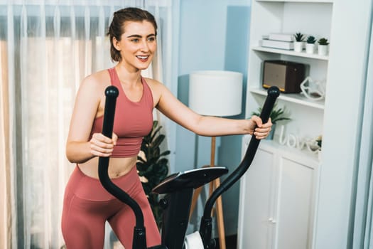 Athletic and sporty woman running on elliptical running machine during home body workout exercise session for fit physique and healthy sport lifestyle at home. Gaiety home exercise workout training.