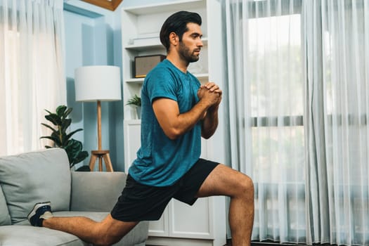 Athletic and sporty man doing squat during home body workout exercise session for fit physique and healthy sport lifestyle at home. Gaiety home exercise workout training concept.