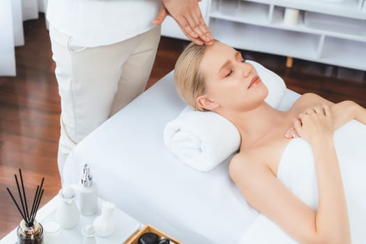 Caucasian woman enjoying relaxing anti-stress head massage and pampering facial beauty skin recreation leisure in dayspa modern light ambient at luxury resort or hotel spa salon. Quiescent