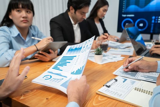 Diverse group of business analyst team analyzing financial data report. Finance data analysis chart and graph dashboard show on TV screen in meeting room for strategic marketing planning. Habiliment