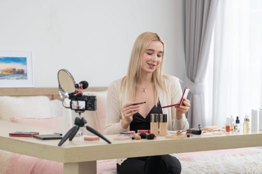 Young woman making beauty and cosmetic tutorial video content for social media. Beauty blogger smiles to camera while showing how to beauty care to audience or followers. Blithe