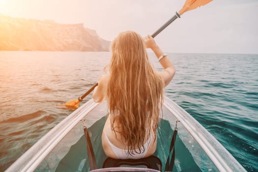 Woman in kayak back view. Happy young woman with long hair floating in transparent kayak on the crystal clear sea. Summer holiday vacation and cheerful female people having fun on the boat.