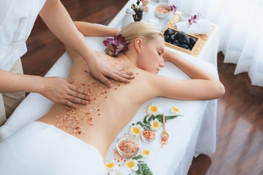 Woman customer having exfoliation treatment in luxury spa salon with warmth candle light ambient. Salt scrub beauty treatment in health spa body scrub. Quiescent