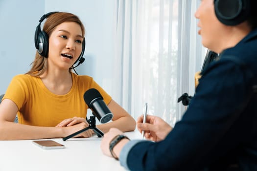 Smiling radio influencer host wearing headphone interviewing woman speaker sharing information to listeners on social media online website live streaming channel at morning at studio record. Infobahn.