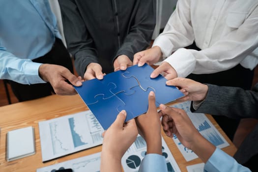 Corporate officer worker collaborate in office, connecting puzzle pieces with report paper on table as partnership and teamwork. Unity and synergy in business concept by merging jigsaw puzzle. Concord