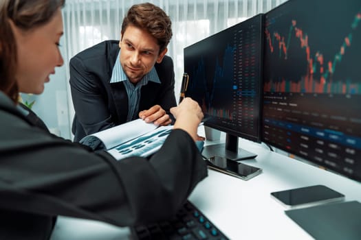 Two business traders discussing value business statistic graph company on paper report analyzing with dynamic stock exchange market currency real time website surround pc screens at office. Postulate.