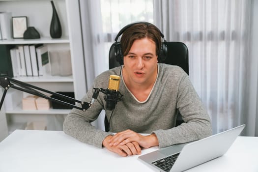 Host channel in smiling smart broadcaster recording, talking show with script and smartphone on desk on live social media, wearing headphones to record video streamer at modern home studio. Pecuniary.