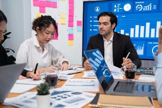 Diverse group of business analyst team analyzing financial data report. Finance data analysis chart and graph dashboard show on TV screen in meeting room for strategic marketing planning. Habiliment