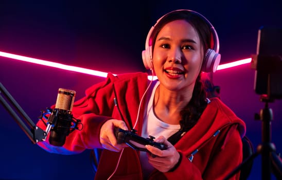 Host channel of smiling beautiful Asian girl streamer with joystick playing online game wearing headphones paste talking with viewers media online. Esport skilled team players in neon room. Stratagem.