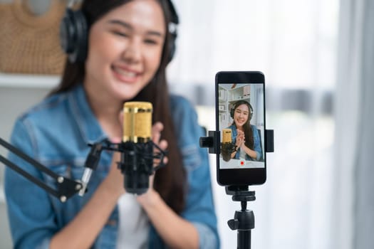 Host channel Asian influencer talking in broadcast wearing headsets on social media live on smartphone recording online, greeting listeners with coaching life or business at modern studio. Stratagem.