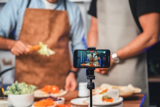 Cropped view of chef influencers presenting fresh salad roll on cooking step by step, streaming via smartphone on social media live channel, showing ingredients vegetable soft tortilla wrap. Sellable.