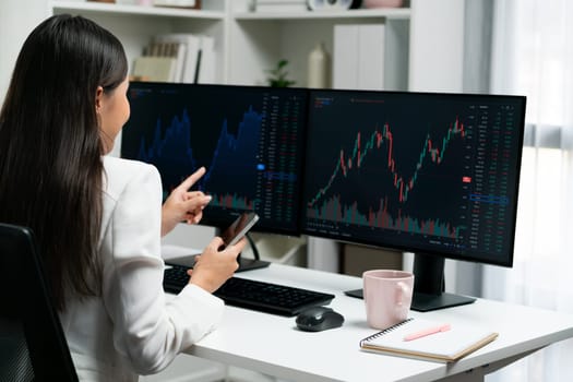 Young beautiful Asian businesswoman looking on pc to analyze profitable of exchange stock market graph at modern office. Concept of investing high profit in wealth security in finance. Stratagem.