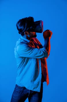 Caucasian man with VR glasses equipment moving in golf playing gesture while standing at neon background. Professional gamer enter in virtual world with futuristic technology innovation. Deviation.