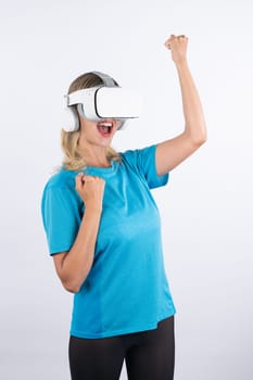 Caucasian happy girl wearing VR glasses and making winner gesture. Skilled woman celebrate while winning game by using VR headsets and standing at pink background. Technology innovation. Contraption.