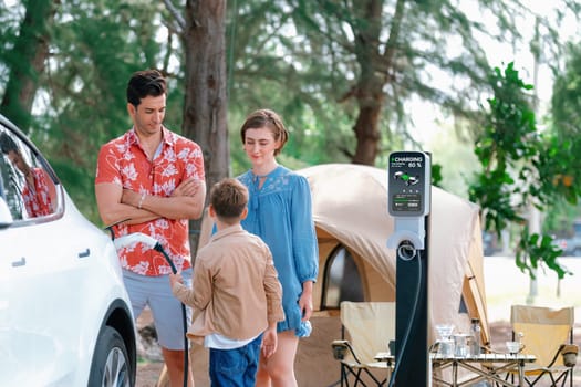 Outdoor adventure and family vacation camping in nature travel by eco friendly car for sustainable future. Lovely family recharge EV car with EV charging station in campsite. Perpetual