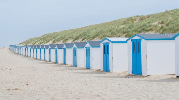 A charming row of blue and white beach huts standing tall on the sandy shores, creating a picturesque scene against the clear blue sky. De Koog beach Texel