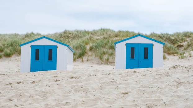 Two colorful beach huts with bright blue doors stand out against the sandy shore, creating a picturesque scene on the coast of Texel, Netherlands.